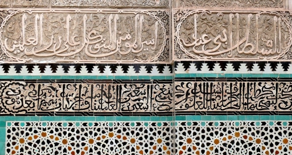 A wall with carved stucco and painted tiles, featuring intricate geometric motifs and Arabic calligraphy